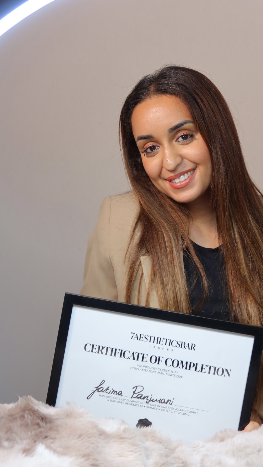 A lash artist smiles while holding her 7AestheticsBar course certificate